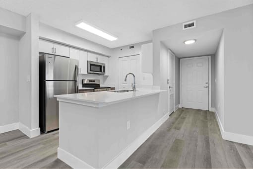 Open kitchen with large island, stainless steel appliances and black fixtures.