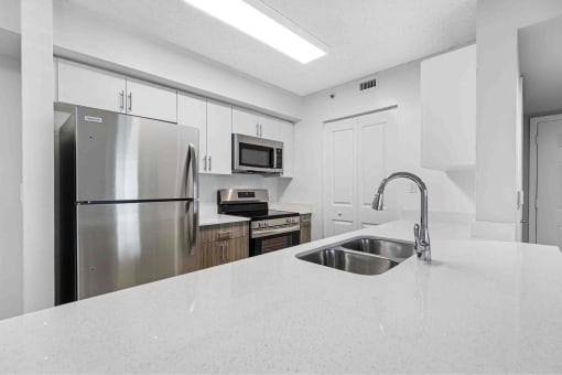 Open kitchen with large island, stainless steel appliances and black fixtures.