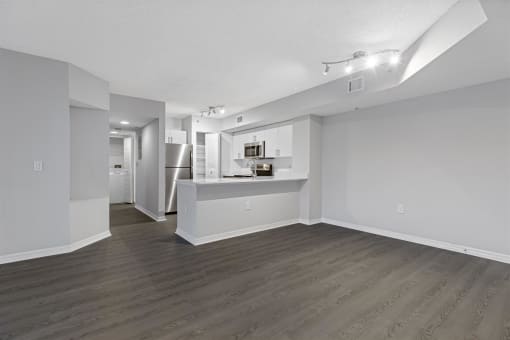 the living room and kitchen of an apartment with white walls and wood flooring