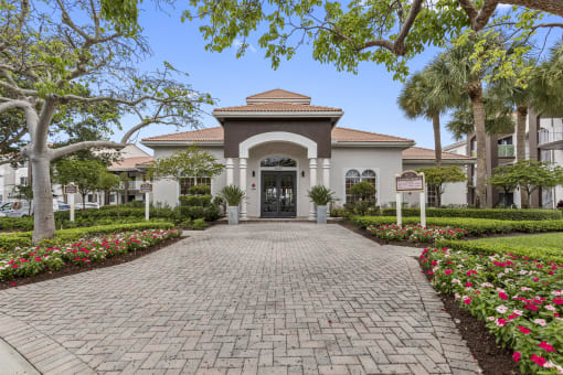 Exterior of leasing office and main building of property with cobblestone path and palm trees