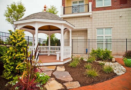 A gazebo is surrounded by a garden and a black fence.