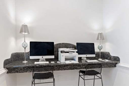 Two computers on a desk with two lamps on either side.