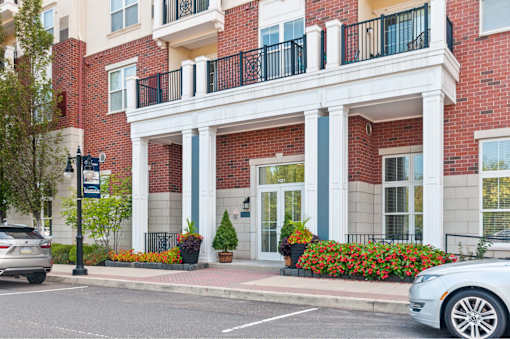 A red brick building with a white balcony and a white car parked in front.