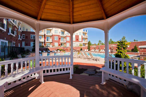 A wooden gazebo with a pool in the background.
