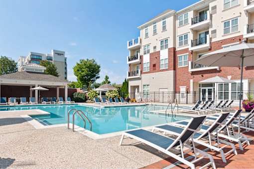 A pool with sun loungers and a building in the background.