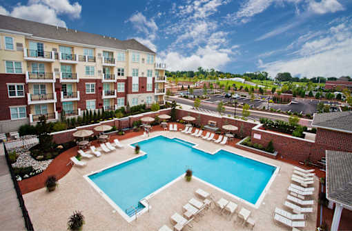 A large swimming pool surrounded by lounge chairs and apartment buildings.