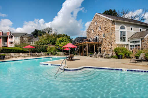 A swimming pool with a stone building and red umbrellas in the background.