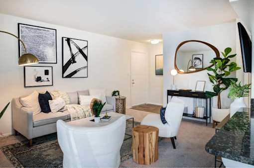 A living room with a grey couch, white chairs, and a black and white artwork on the wall.
