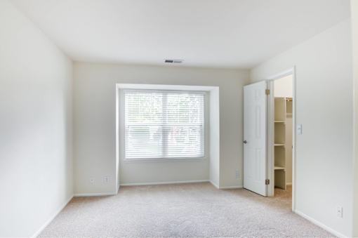 A room with a carpeted floor and a window with blinds.