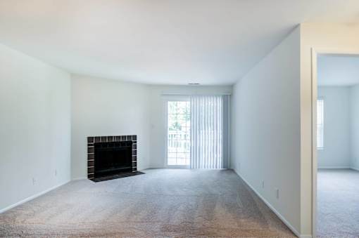 A large, empty room with a fireplace and carpeted floor.