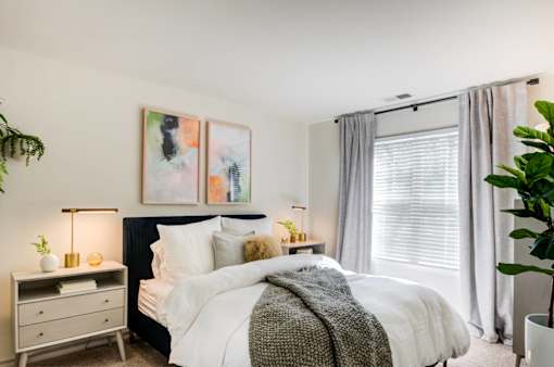 A bedroom with a large bed, a nightstand with a lamp, and a painting on the wall.