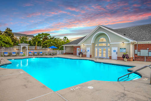 A swimming pool in front of a building with a sunset in the background.