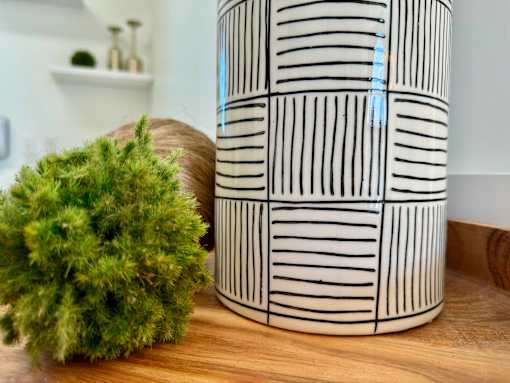 A decorative vase with black and white stripes sits on a wooden table.