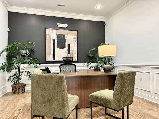 A room with a desk, two chairs, and a painting on the wall.