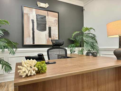 A wooden desk with a black chair and a painting on the wall.