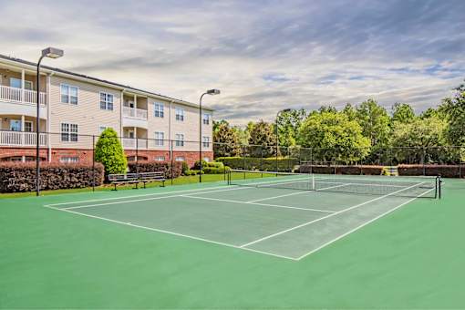 A tennis court is surrounded by apartment buildings.