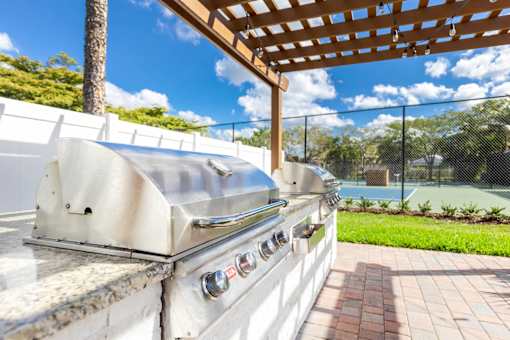 A stainless steel grill is on a patio with a wooden pergola overhead.