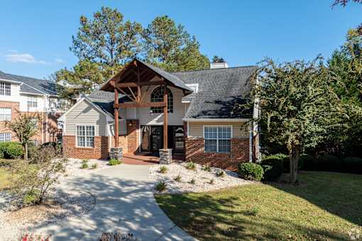 A house with a brown roof and a white door is surrounded by greenery.