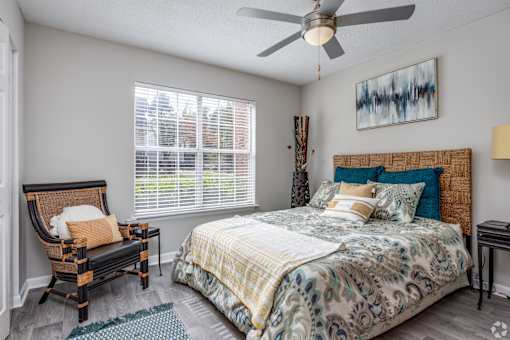 A bedroom with a bed, chair, and a painting on the wall.