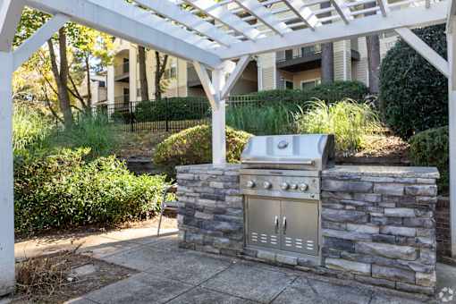 A BBQ grill is built into a stone wall under a white pergola.