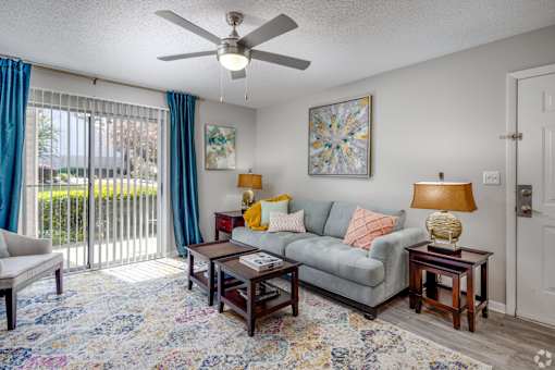 A living room with a grey couch, a rug, and a ceiling fan.