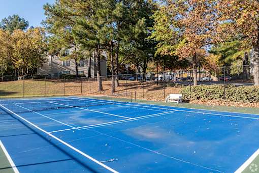 A blue tennis court surrounded by trees and a fence.