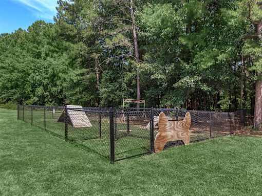 A dog house is behind a chain link fence in a grassy area.