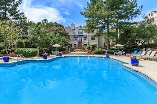 A large blue swimming pool surrounded by trees and lounge chairs.