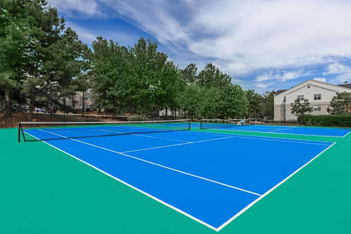 A blue tennis court surrounded by trees and a building.