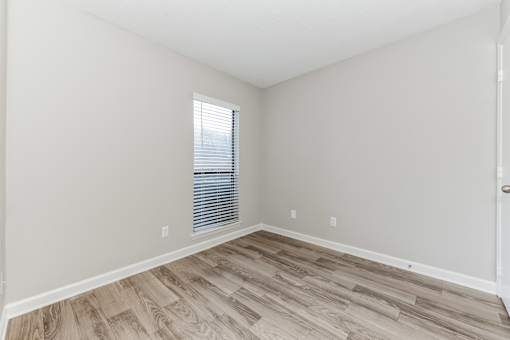 A room with wooden flooring and a window with blinds.