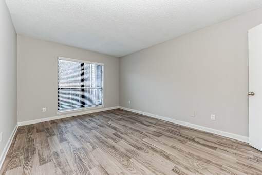 A room with wooden flooring and a window with blinds.