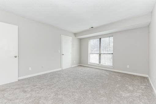 A room with a carpeted floor and a window with blinds.