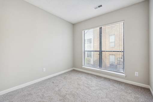A room with a carpeted floor and a window with blinds.