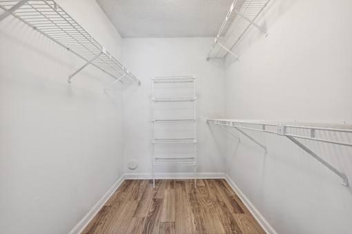 A white walk-in closet with shelves and a wooden floor.