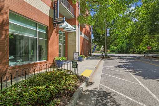 1-Bedroom Apartments in Nashville, TN - The Marquee at Belle Meade - Parking Area of the Brick Apartment Building With Property Sign, Landscaped Planters, Parking Spaces, and Mature Trees.