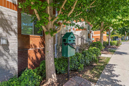 A green mailbox is attached to a metal pole on a sidewalk.