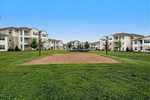 A baseball diamond in the middle of a grassy field with apartment buildings in the background.