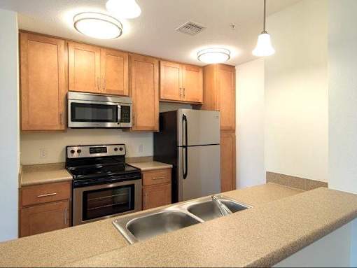Kitchen bar view showing light maple cabinetry, light beige faux granite counters with sink and stainless appliances