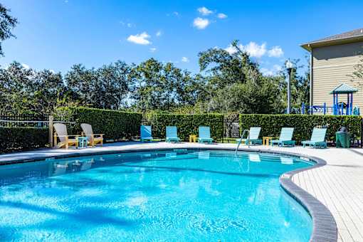 A swimming pool surrounded by trees and chairs.