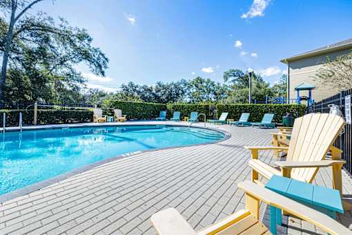 A sunny day at the pool with chairs and a bench.