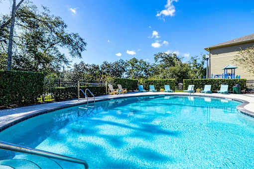 A large outdoor swimming pool surrounded by trees and lounge chairs.