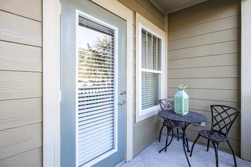 A small table with a green bottle on it sits on a porch.
