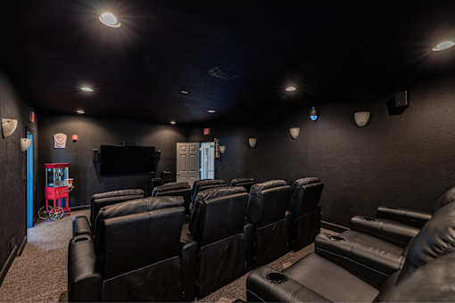 A dark room with a row of black leather chairs and a television mounted on the wall.