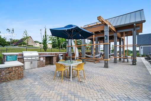 Apartments Near Donelson Nashville TN - The Sound at Pennington Bend - An Outdoor Community Area With Covered Tables And Chairs, A BBQ With Counter Space, And A Couple Hammocks All Surrounded By Green