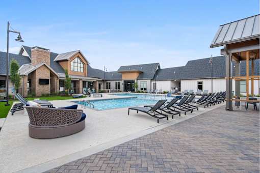 Apartments Nashville, TN - The Sound at Pennington Bend - Swimming Pool with Lounge Tanning Chairs Surrounding the Pool, a Daybed, a Grass Area, and a Mounted TV