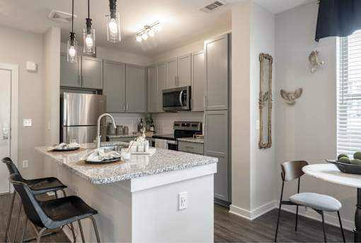 Nashville, TN, Apartments - The Sound at Pennington Bend - Kitchen with Stainless Steel Appliances, Subway Tile Backsplash, Gray Cabinetry, Granite Countertops, Pendant Lighting, and a Kitchen Island.
