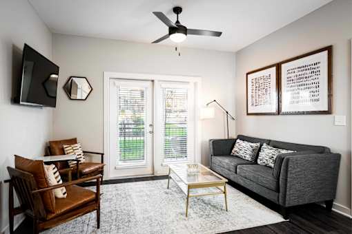 Apartments for Rent in Nashville, TN - The Sound at Pennington Bend - Living Room with Hardwood-Inspired Plank Flooring, Ceiling Fan, Mounted TV, Mirror, Couch, Armchairs, and Glass Doors.