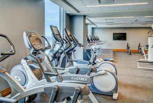 A gym with a row of stationary bikes and a television mounted on the wall.