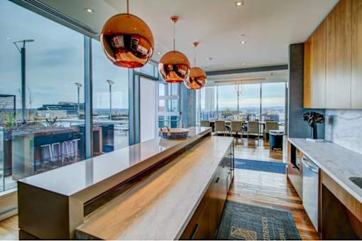 A modern kitchen with a long counter and pendant lights.
