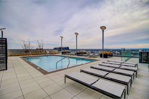 A pool with sun loungers and lights on the side.